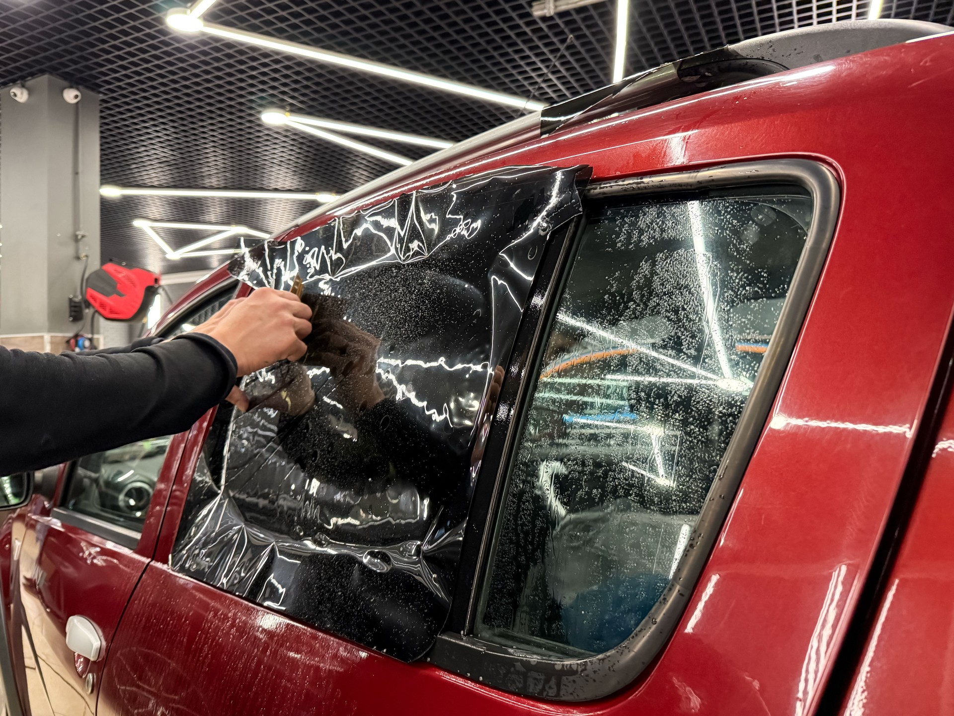 Applying tinting foil on a car window in the tuning studio close-up. Male car service worker glue window tinting in luxury car detailing car repair the concept of love for cars and protection.